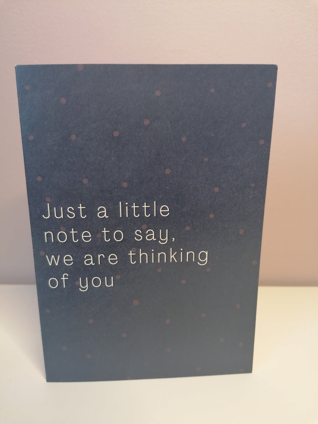 Navy background with a subtle polka dot design, white text Just a little note to say we are thinking of you.