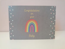 Load image into Gallery viewer, Rainbow baby cars, yellow text on grey background reads congratulations on you (image of a rainbow) baby. There is a simple polka dot motif of yellow, blue and pink dots running down the two sides of the card
