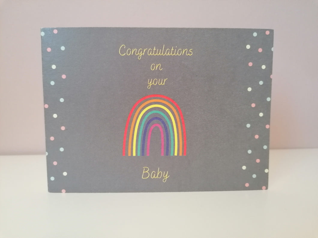 Rainbow baby cars, yellow text on grey background reads congratulations on you (image of a rainbow) baby. There is a simple polka dot motif of yellow, blue and pink dots running down the two sides of the card